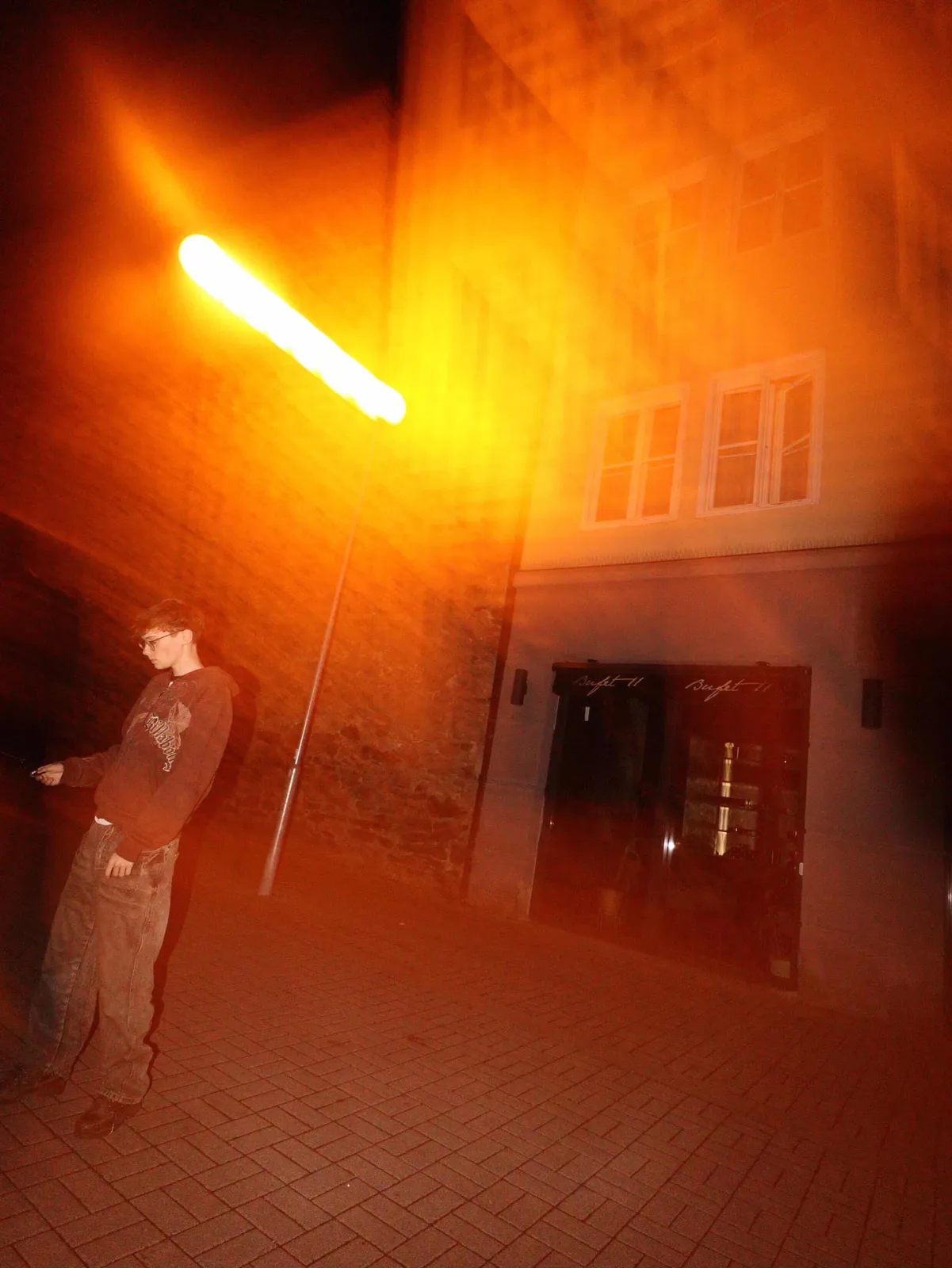Filip v brýlích pod lampou, přes záběr jde oranžová záře